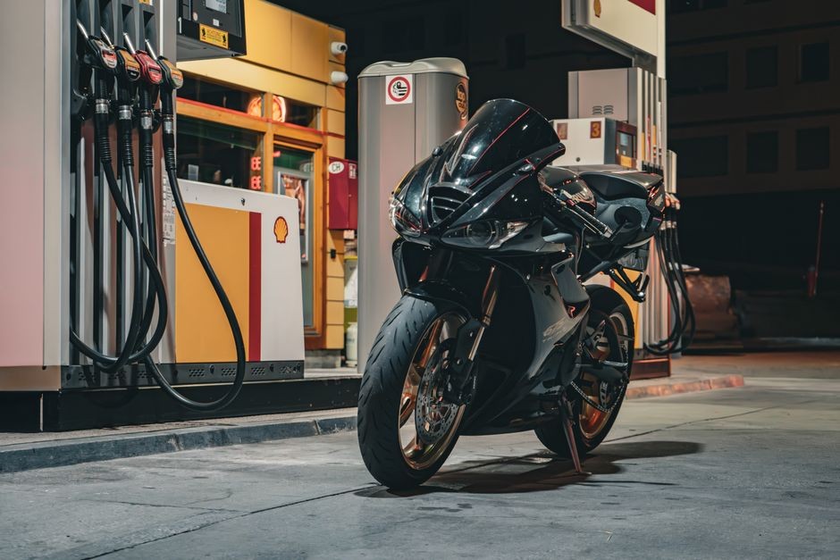 Sebuah motor sport hitam yang ramping diparkir di stasiun Shell pada malam hari.