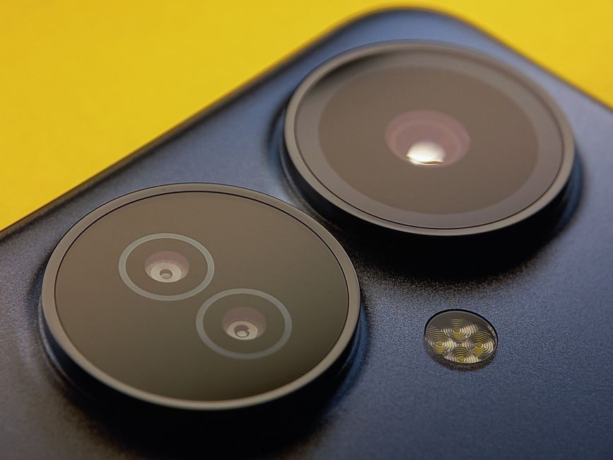 Dekat sekali lensa kamera smartphone dengan latar belakang kuning cerah, menampilkan teknologi modern.