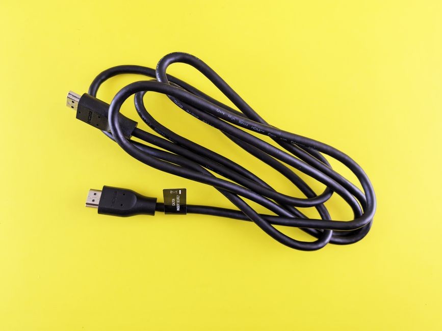 Sebuah kabel HDMI hitam yang digulung rapi ditampilkan di permukaan kuning cerah, ideal untuk visual teknologi.