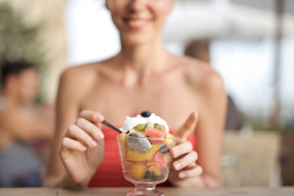 Wanita bahagia yang makan salad buah di kafe, menikmati pencuci mulut yang segar.