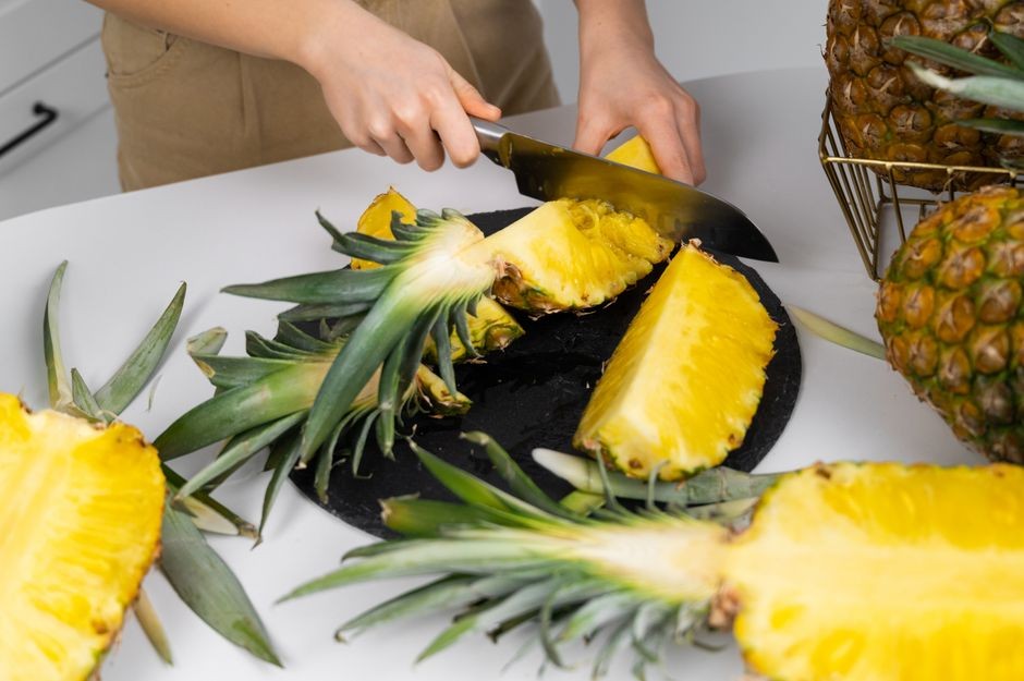Wanita mengiris nanas yang matang di meja dapur, menunjukkan kesegaran dan persiapan makanan sehat.