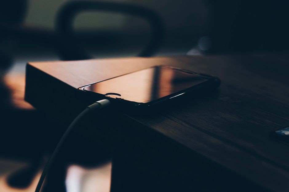 Smartphone yang terhubung ke charger di atas meja kayu untuk menggambarkan rutinitas mengisi daya perangkat harian.