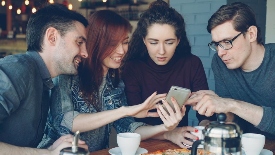 Dua orang teman sedang melihat layar smartphone bersama di meja santai