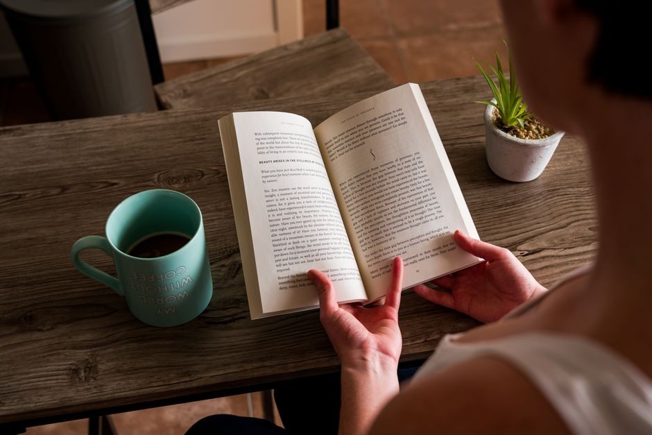 Seseorang menikmati buku dengan cangkir kopi di atas meja kayu sebagai jeda sehat dari layar ponsel