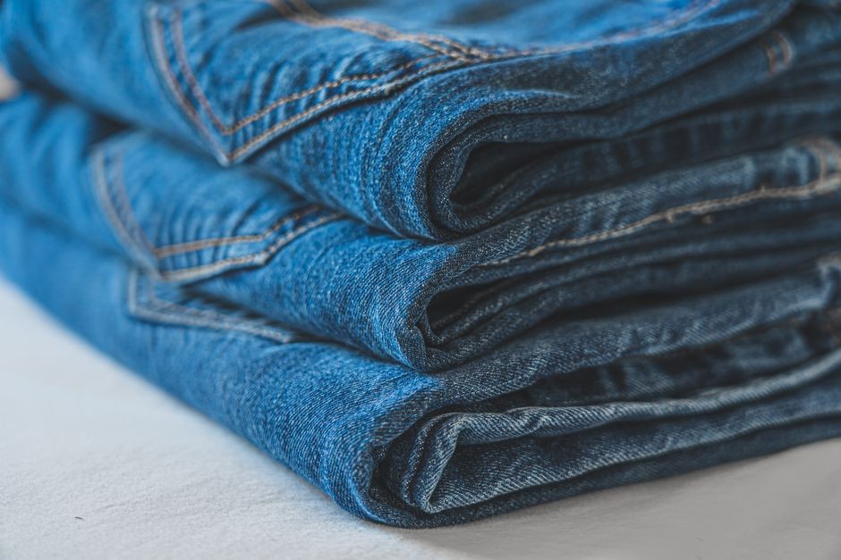 Tumpukan celana jeans denim biru yang dilipat rapi menampilkan tekstur dan jahitan.