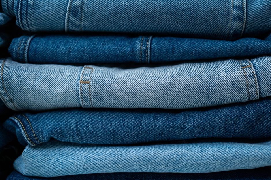Tampilan close-up dari celana jeans denim biru yang ditumpuk, menampilkan berbagai nuansa kain indigo.