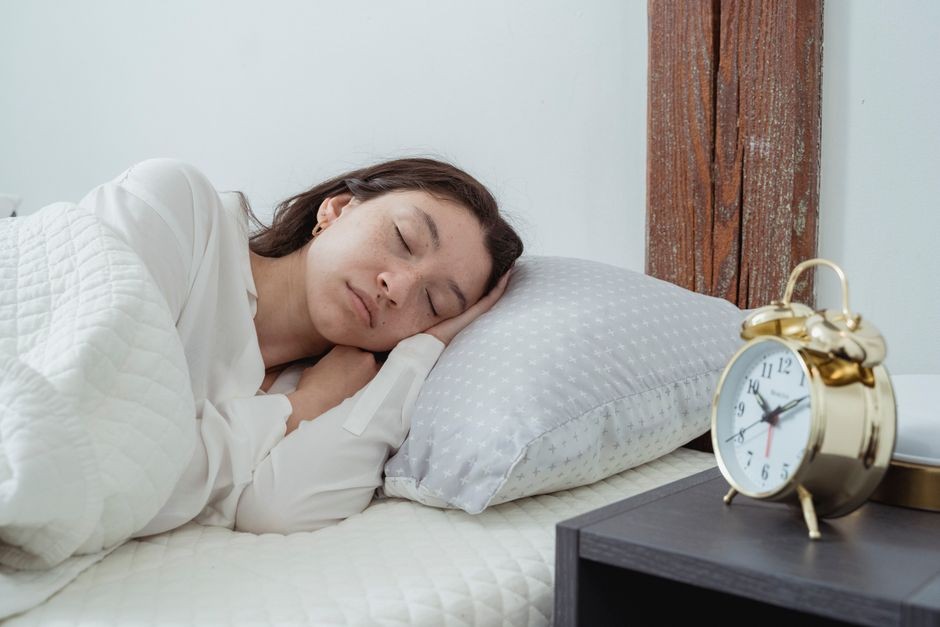 Perempuan muda tidur dengan tenang di tempat tidur dengan jam weker vintage di dekatnya.