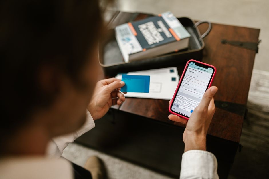 Orang yang melakukan pembayaran online menggunakan smartphone dan kartu kredit di dalam ruangan.