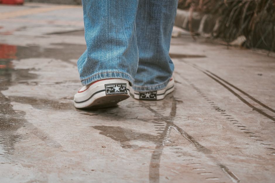 Sepatu sneakers basah tergenang air hujan di aspal jalan, ilustrasi sepatu kehujanan