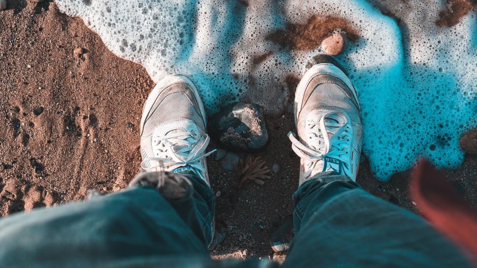 Seseorang sedang menyikat sneakers putih dengan busa sabun untuk mengangkat noda lumpur