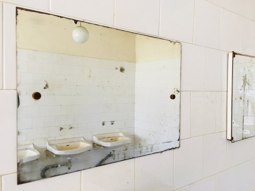 Lapisan keramik kamar mandi lembap dengan noda jamur dan lumut di sela-sela nat