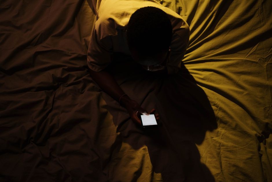 Tangan menggulir layar ponsel dalam kamar gelap di malam hari