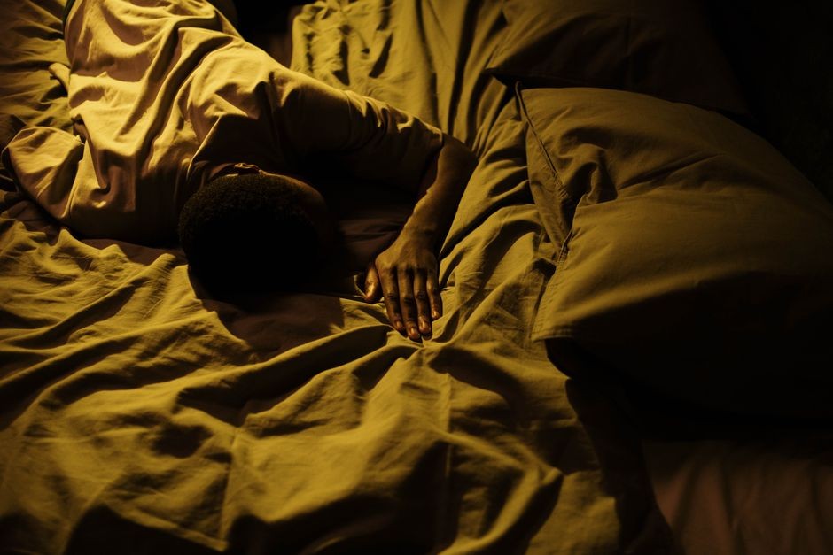 Seseorang tertidur pulas di bawah selimut dalam kamar gelap, ilustrasi tidur nyenyak yang ideal bagi ritme sirkadian