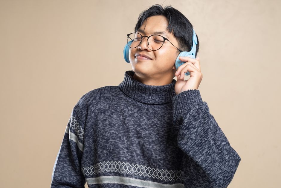 Seorang pria muda dengan sweater yang nyaman mendengarkan musik dengan headphone, merasa santai dan bahagia.