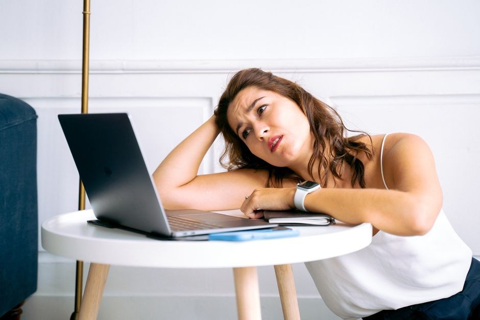 Orang memegang kepala sambil menatap layar laptop, tampak bingung