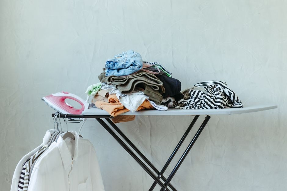 Setrika listrik di atas papan setrika bersama tumpukan baju