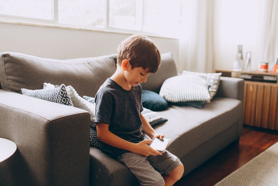 Anak muda duduk di sofa sambil main ponsel, gambaran pola hidup sedentari atau mager
