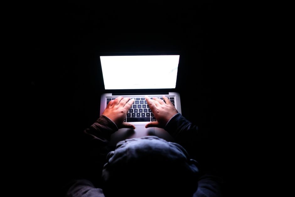 Seseorang mengetik di laptop dengan layar gelap menampilkan kode dan rekaman pengawasan