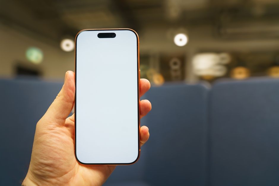 Tangan menggenggam smartphone modern berlayar lengkung mulus, keindahan visual yang sering dipasangi pelindung berisiko