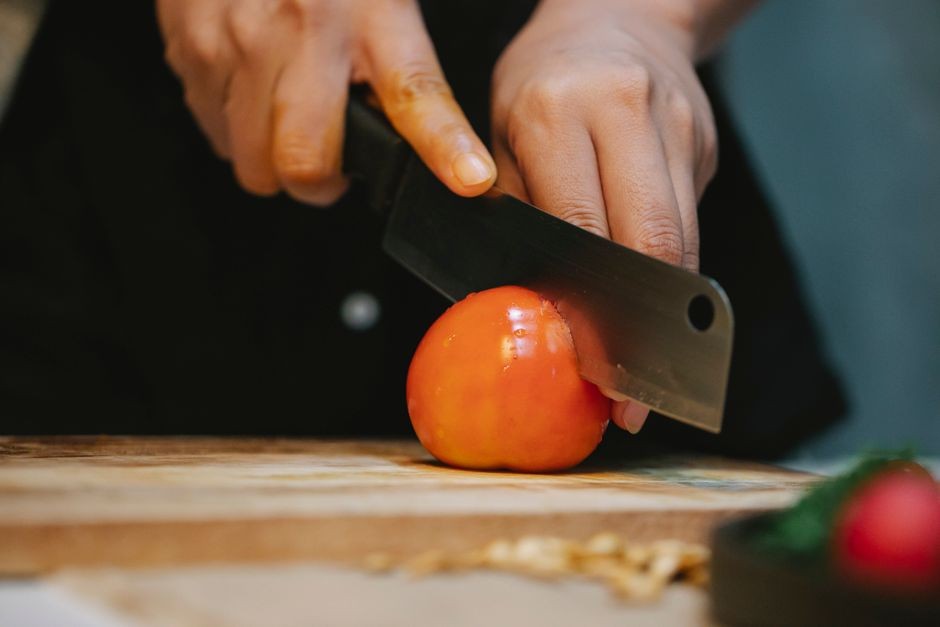 Bilah pisau dapur yang tajam mengiris tomat segar dengan rapi tanpa merusak tekstur daging buah