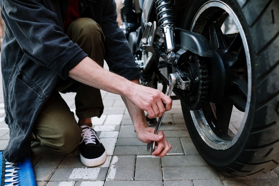 Mekanik memeriksa dan menyetel kekencangan rantai motor dengan kunci pas di bengkel