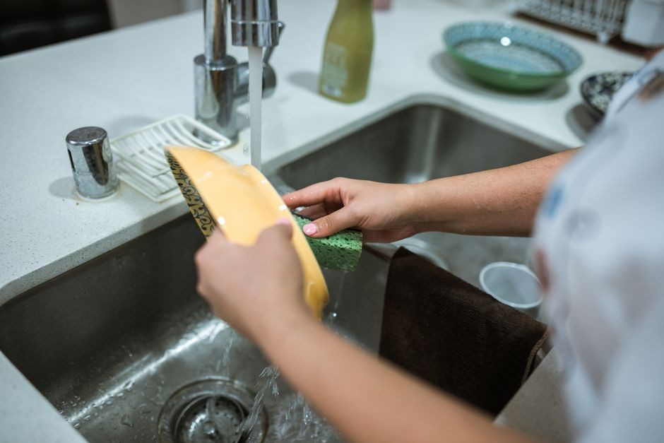Seseorang mencuci peralatan masak di wastafel dapur menggunakan spons berbusa lembut dan air mengalir