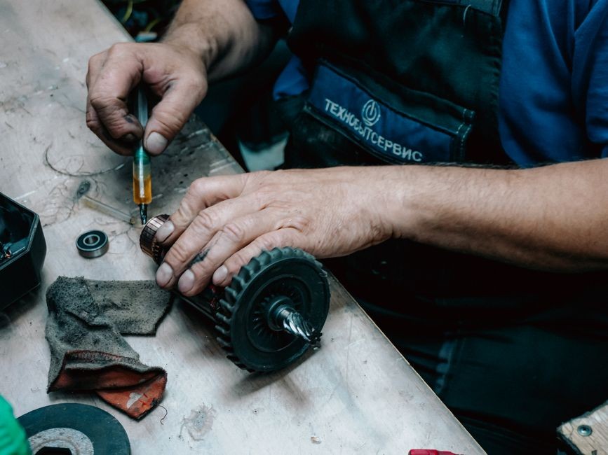 Tangan teknisi membongkar penutup motor dan membersihkan komponen penggerak menggunakan obeng