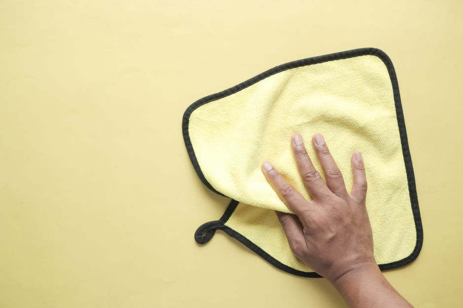Seseorang menyeka dan mengeringkan permukaan bodi smartphone memakai kain microfiber bersih