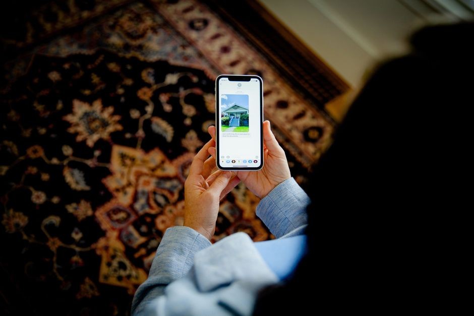 Pandangan dari atas orang yang menggunakan smartphone untuk melihat foto sebuah rumah di dalam ruangan