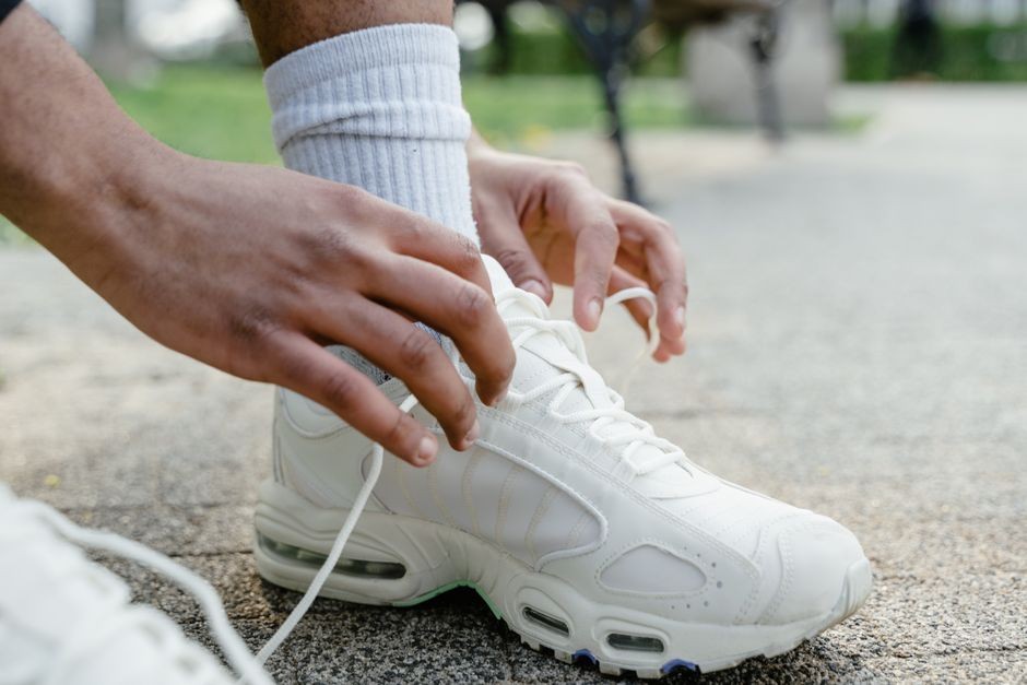 Seseorang sedang menyikat dan membersihkan sepatu putih dari noda tanah