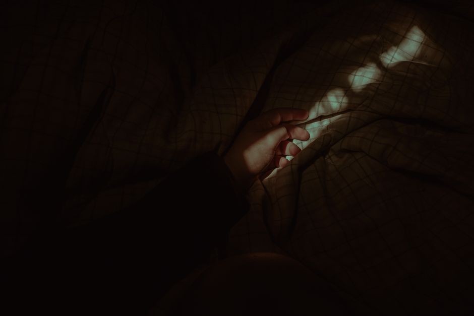 Cahaya layar ponsel menyinari wajah di kamar gelap menjelang tidur