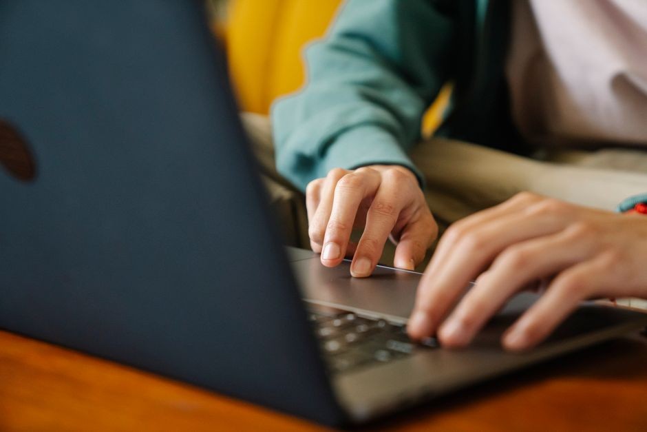Individu yang mengetik di laptop, fokus pada tangan dan keyboard dalam pengaturan dalam ruangan.