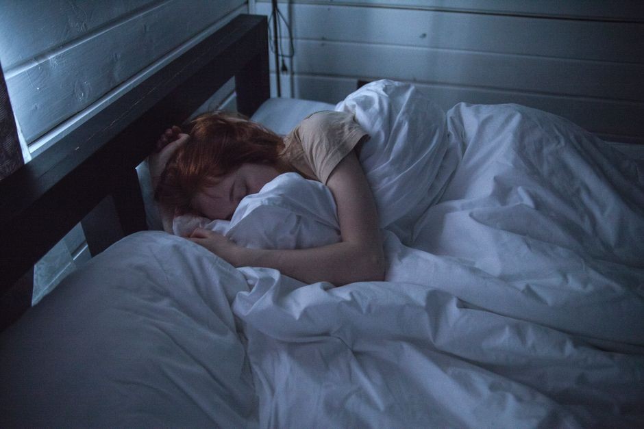 Seorang wanita yang tidur dengan tenang di dalam kamar yang nyaman, terbungkus oleh seprai putih lembut, di bawah cahaya lembut lampu malam.