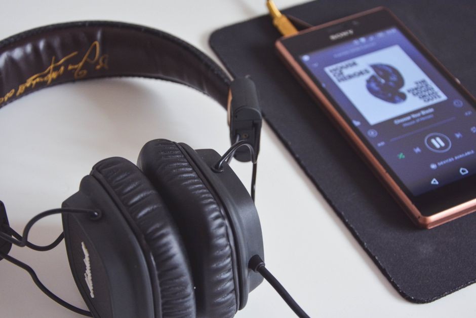 Headphone diletakkan di samping layar smartphone yang memutar lagu