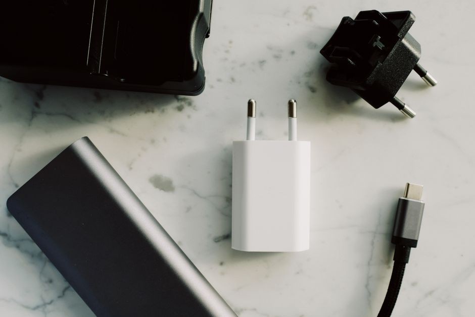 Koleksi adaptor dan pengisi daya elektronik yang menampilkan USB-C dan konektor lainnya di permukaan marmer.
