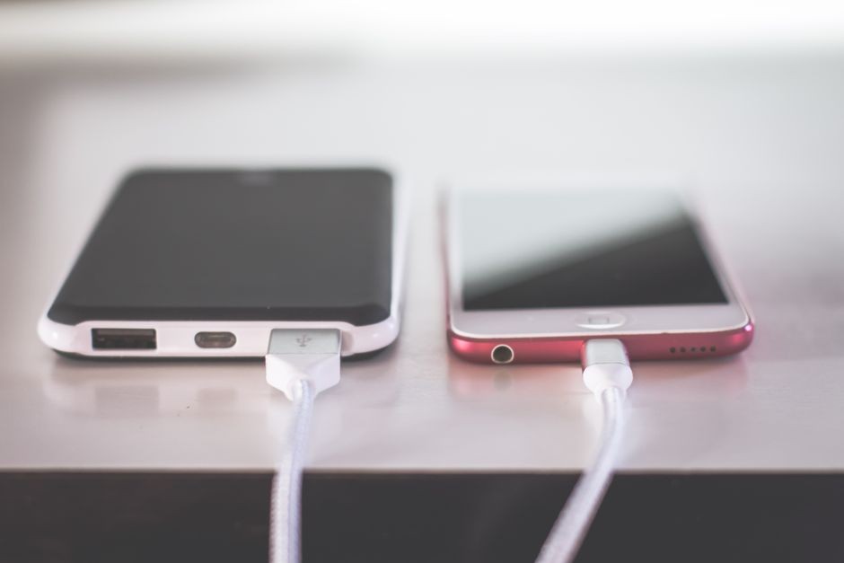Dua smartphone yang sedang mengisi daya dengan kabel charger di atas meja kayu.