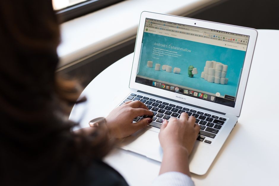 Pengusaha wanita bekerja di laptop dengan halaman web Android 6.0 Marshmallow terbuka.