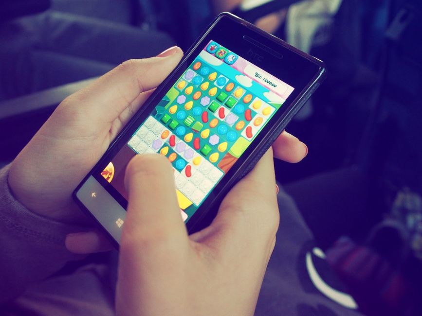 Tangan yang memegang smartphone dengan permainan puzzle berwarna-warni di layar, menampilkan teknologi modern.