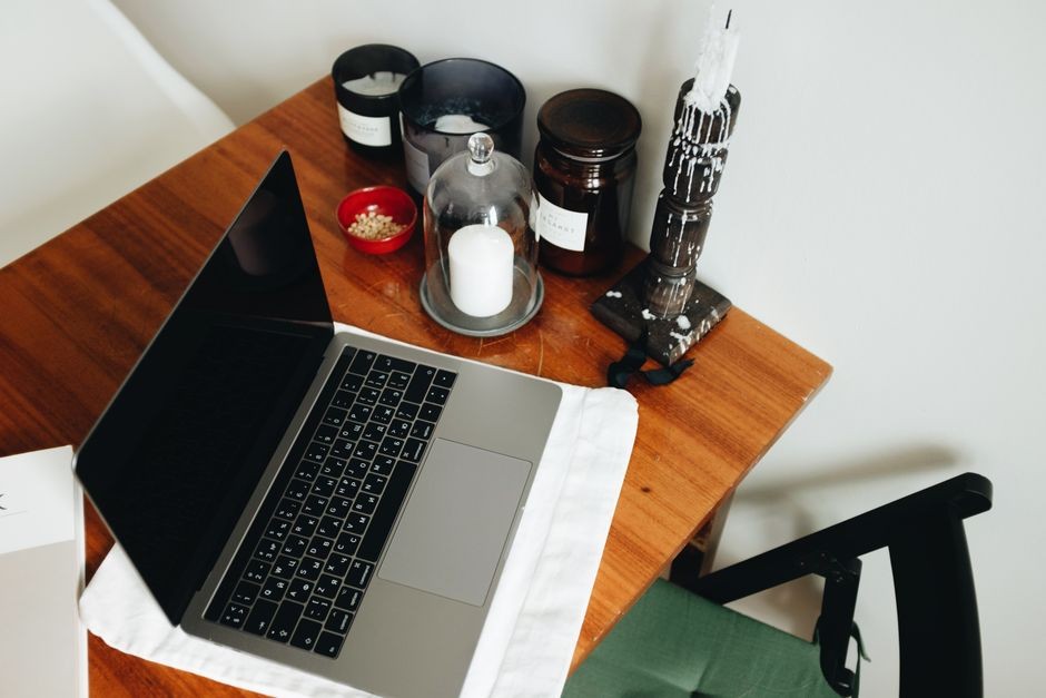Sebuah kantor rumah dengan laptop di meja kayu, dikelilingi oleh lilin dan stoples untuk suasana yang hangat.