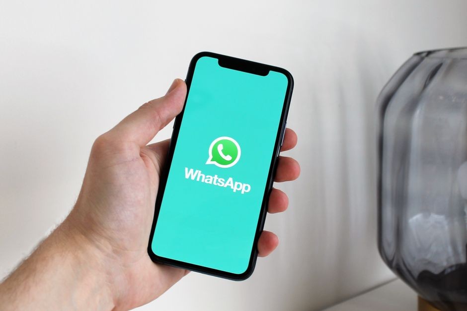 Close-up tangan yang memegang smartphone yang menampilkan layar aplikasi WhatsApp.