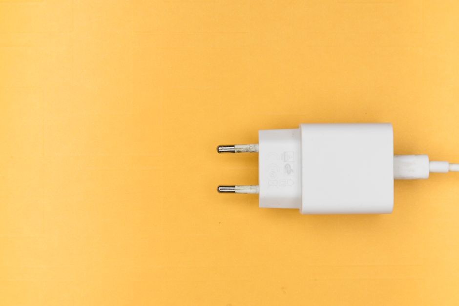 Colokan charger putih di latar belakang kuning bersih, sempurna untuk tema teknologi.