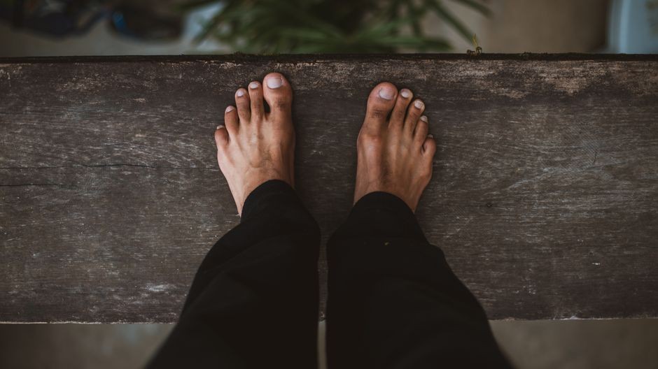 Pandangan dekat kaki telanjang dalam celana hitam berdiri di permukaan kayu.