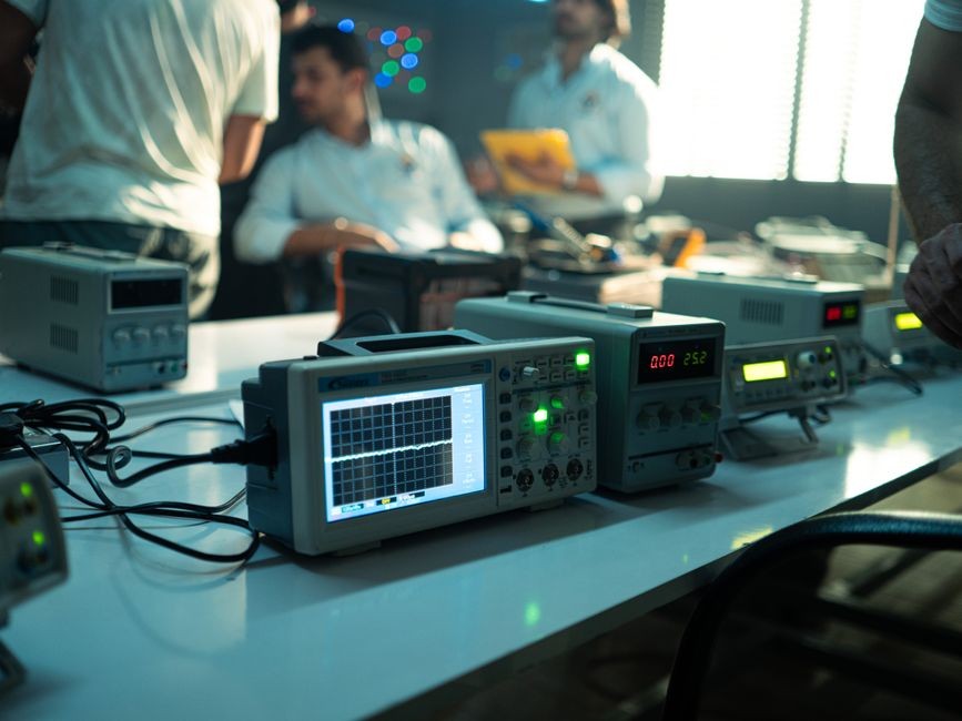Insinyur bekerja di laboratorium elektronik dengan osiloskop dan peralatan lainnya pada hari yang cerah.