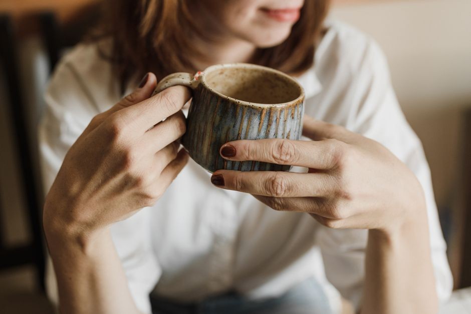 Seseorang yang tampak lelah memegang cangkir kopi saat baru bangun tidur.