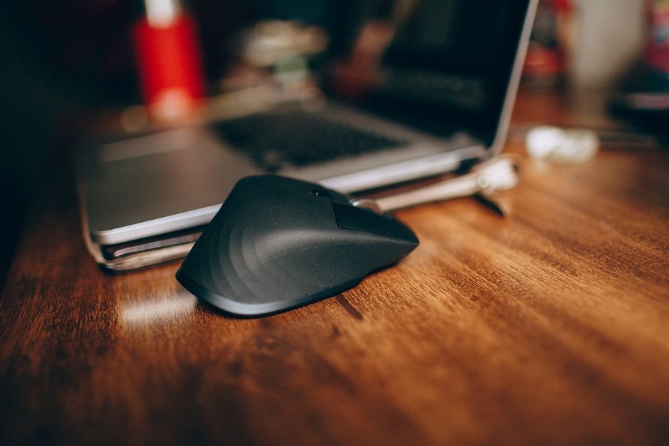 Sebuah mouse nirkabel di samping laptop di atas meja kerja kayu
