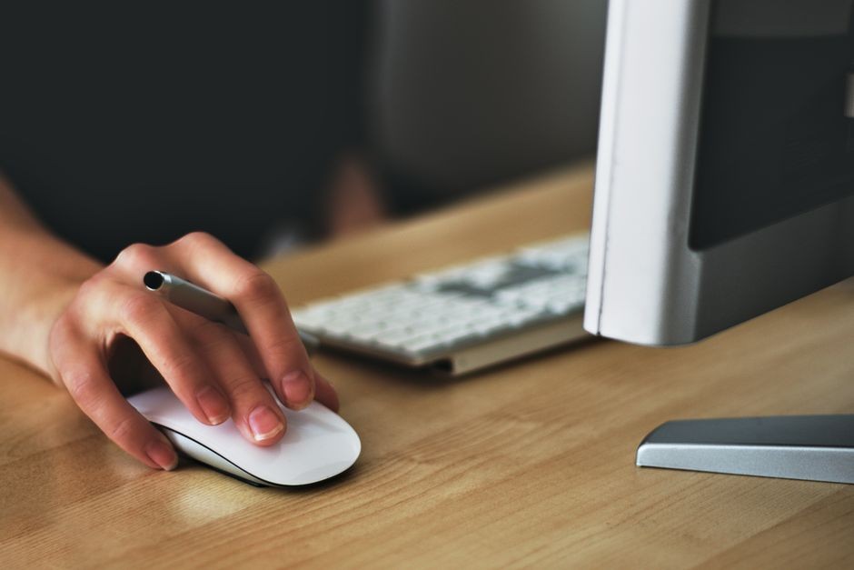 Tangan sedang menggerakkan mouse nirkabel dengan lancar di atas meja komputer