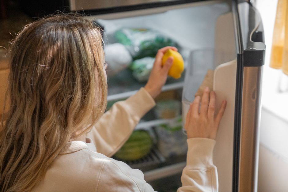 Wanita meraih lemon di kulkas, menggambarkan kebiasaan hidup sehat.