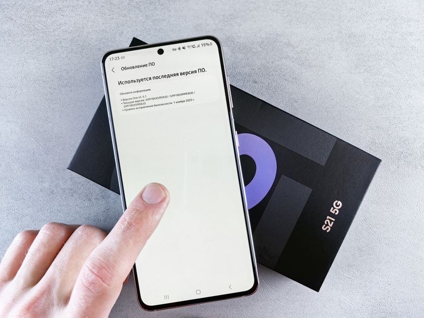 Jari berinteraksi dengan smartphone pada layar pembaruan perangkat lunak di atas kotak ponsel, terpisah di latar belakang terang.