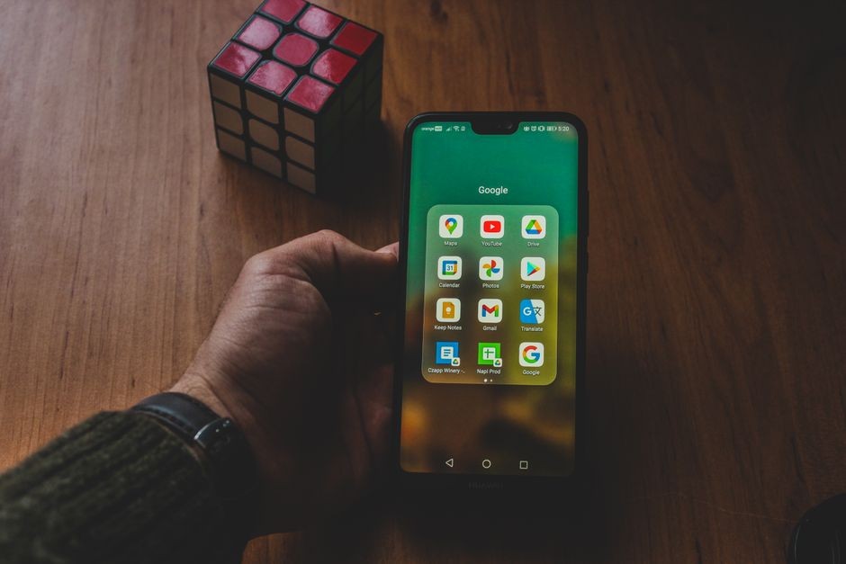 Tangan memegang smartphone Android yang menampilkan layar pengaturan sistem dan aplikasi