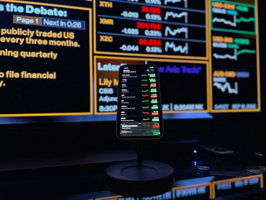 Ponsel pintar menampilkan data pasar saham dengan latar belakang layar keuangan di London.